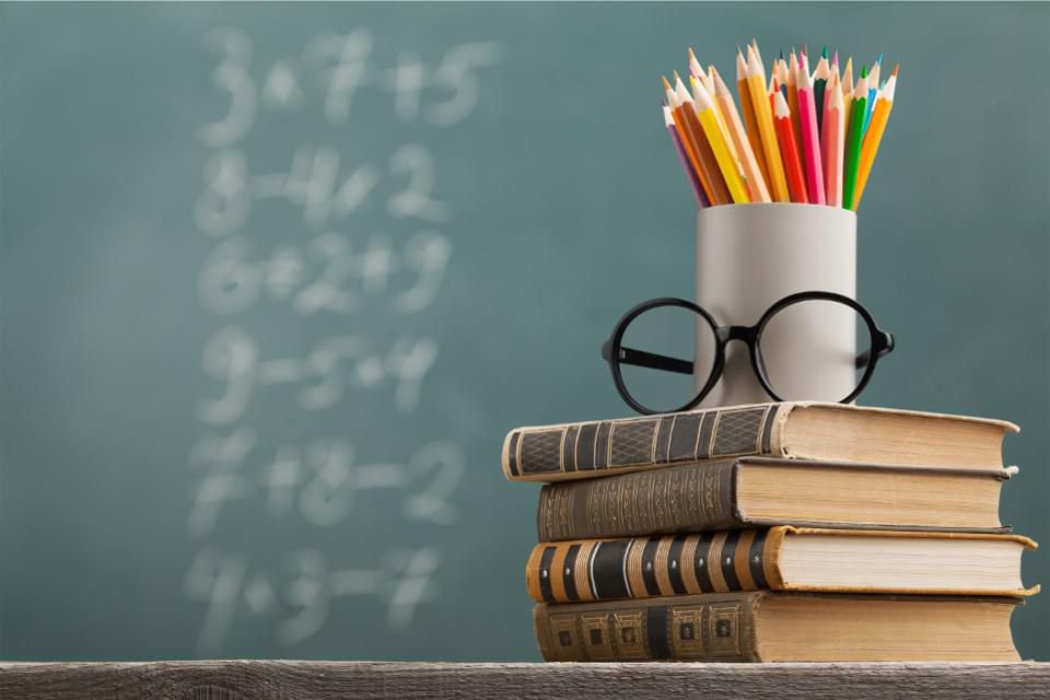 Books stacked with glasses and a cup of pencils on top. Chalkboard background