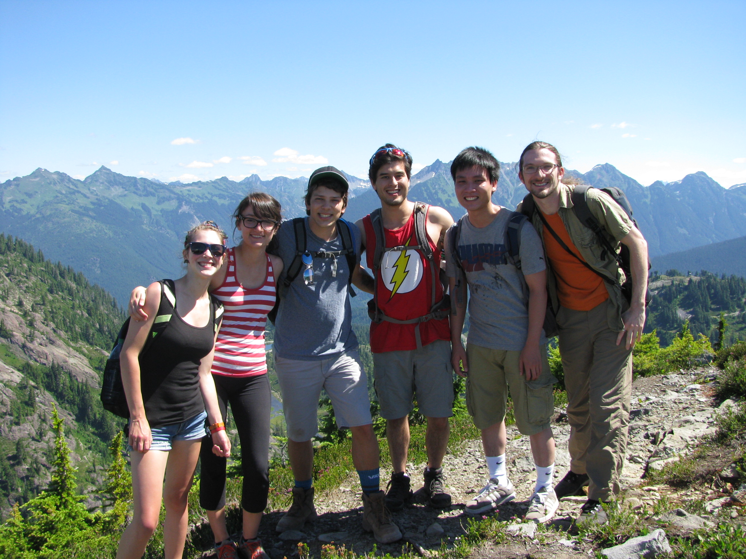a group poses on a mountain with a mountain range and blue sky behind them. Summer 2015 group hike