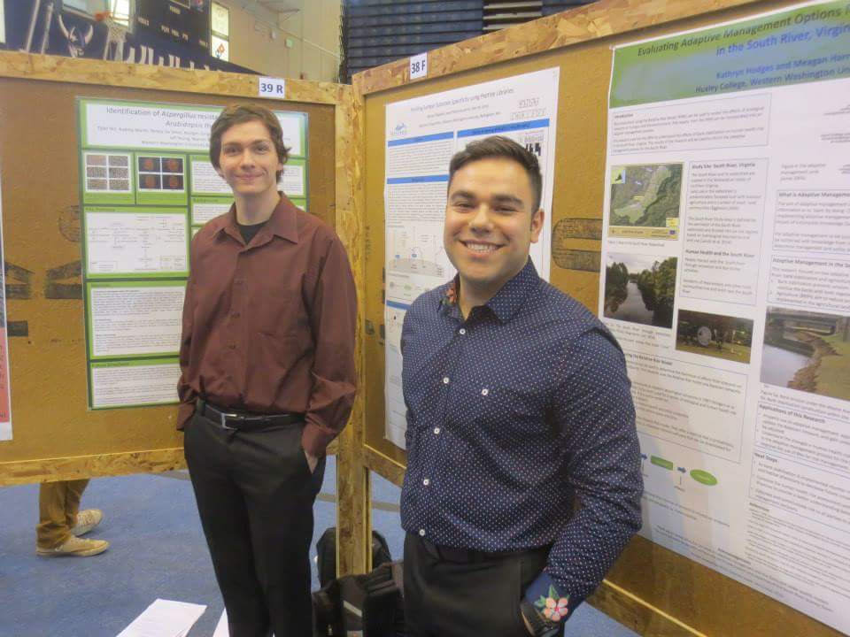 Two students smile in front of their research posters