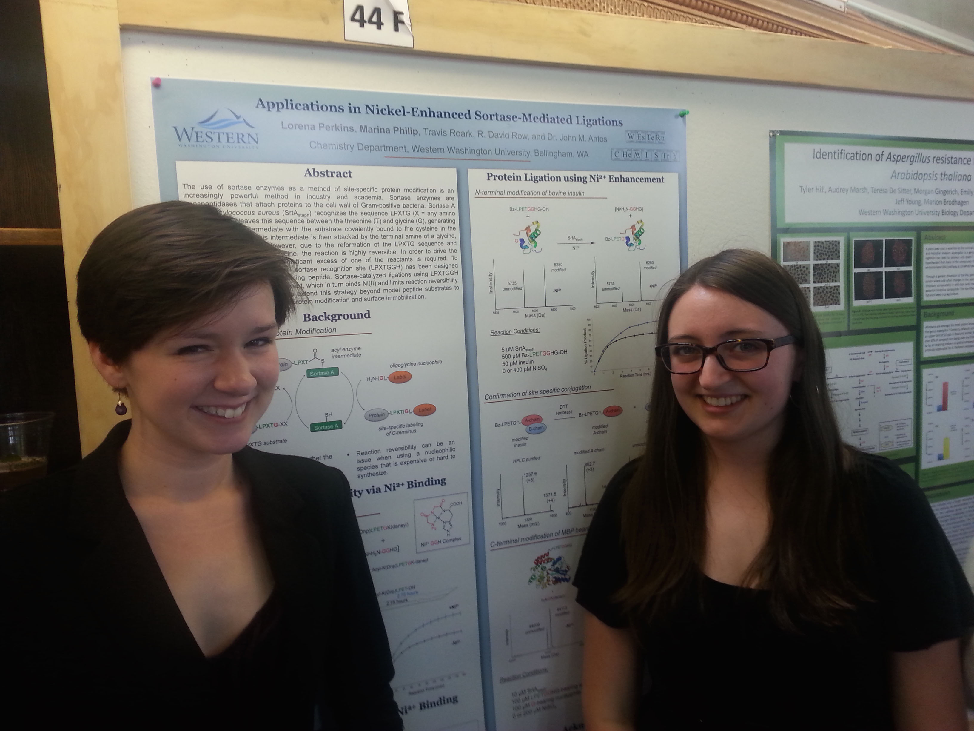 Lorena Perkins and Marina Philip smile in front of their research poster