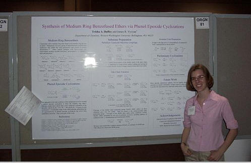 a single student poses beside a poster