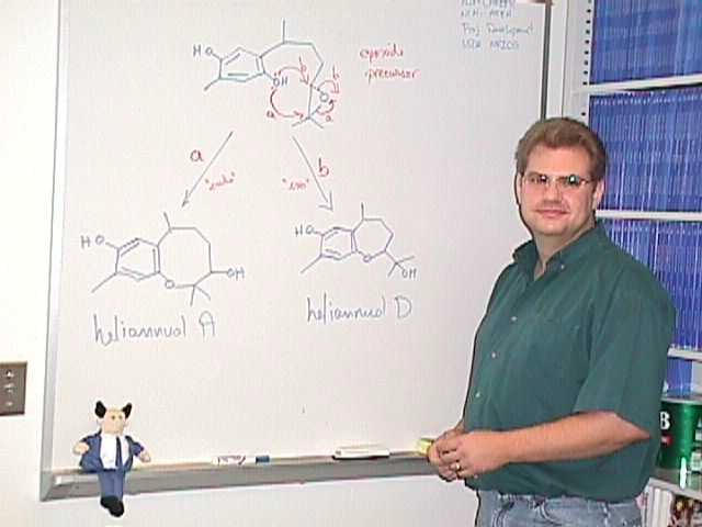 a man stands beside a whiteboard with molecular diagrams written in colorful ink