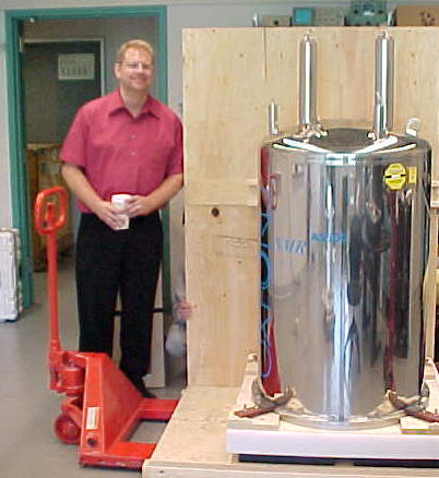 a man poses beside a metal cylindrical object