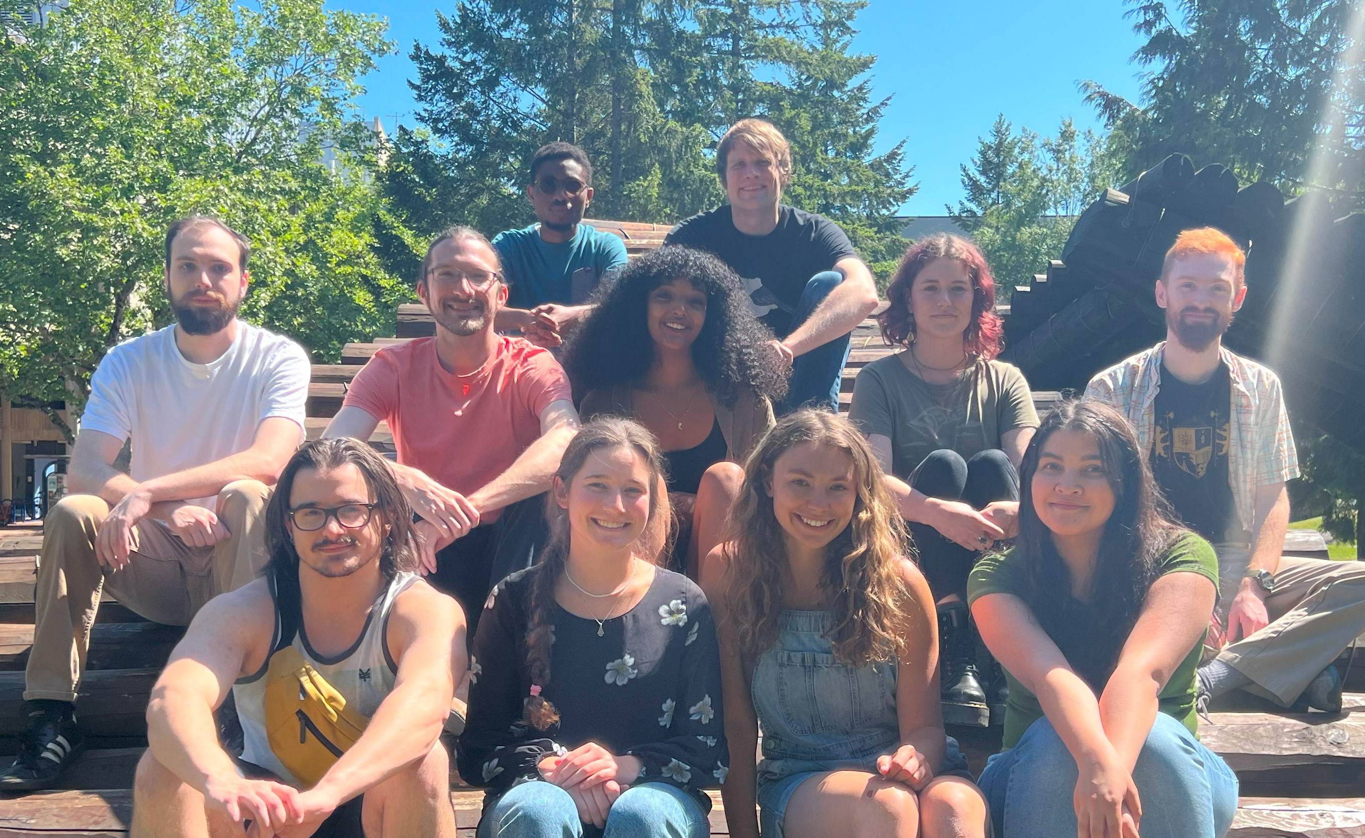 Dr. Kowalczyk and ten research students sitting on the log sculpture outside of Morse Hall, spring 2023