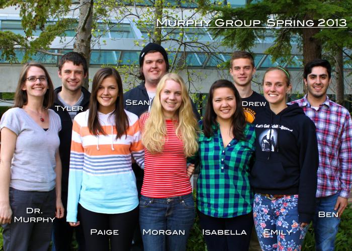 A group of students and Amanda Murphy stand in front of a building, smiling at the camera. The photo is labeled "Murphy Group Spring 2013"