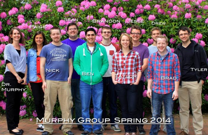 A group of students and Amanda Murphy stand in front of floral plants, smiling at the camera. The picture is labeled "Murphy Group Spring 2014"