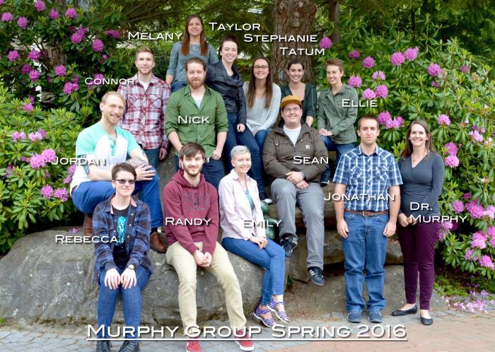 A group of students sit on boulders in front of floral plants, smiling at the camera. The photo is labeled "Murphy Group Spring 2016"