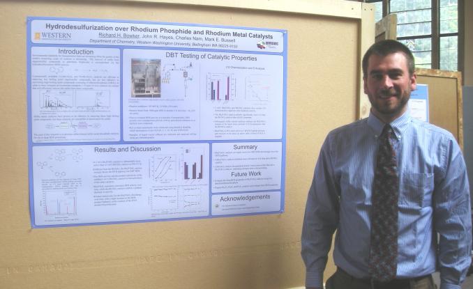 Rick Bowker stands in front of poster at scholars week