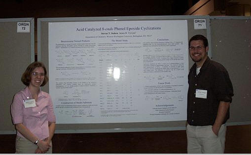 Two students standing beside a poster