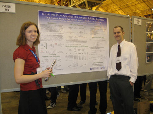 two students pose beside a poster
